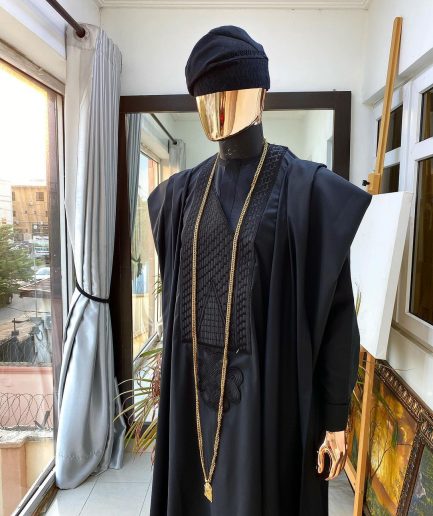 A charcoal black agbada, Jesus piece long fashion chain and hand woven aso oke Yoruba hat.
