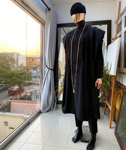 A charcoal black agbada, Jesus piece long fashion chain and hand woven aso oke Yoruba hat.