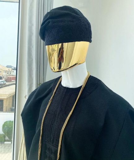 A charcoal black aso dashiki with a floral and box-shaped embroidery design, a hand-weaved Yoruba hat, and a gold Jesus timepiece