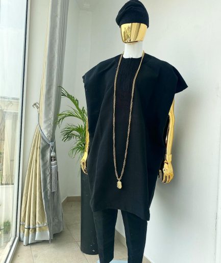A charcoal black aso dashiki with a floral and box-shaped embroidery design, a hand-weaved Yoruba hat, and a gold Jesus timepiece